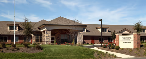 Exterior view of a memory care facility with stone entrance and landscaped front lawn.
