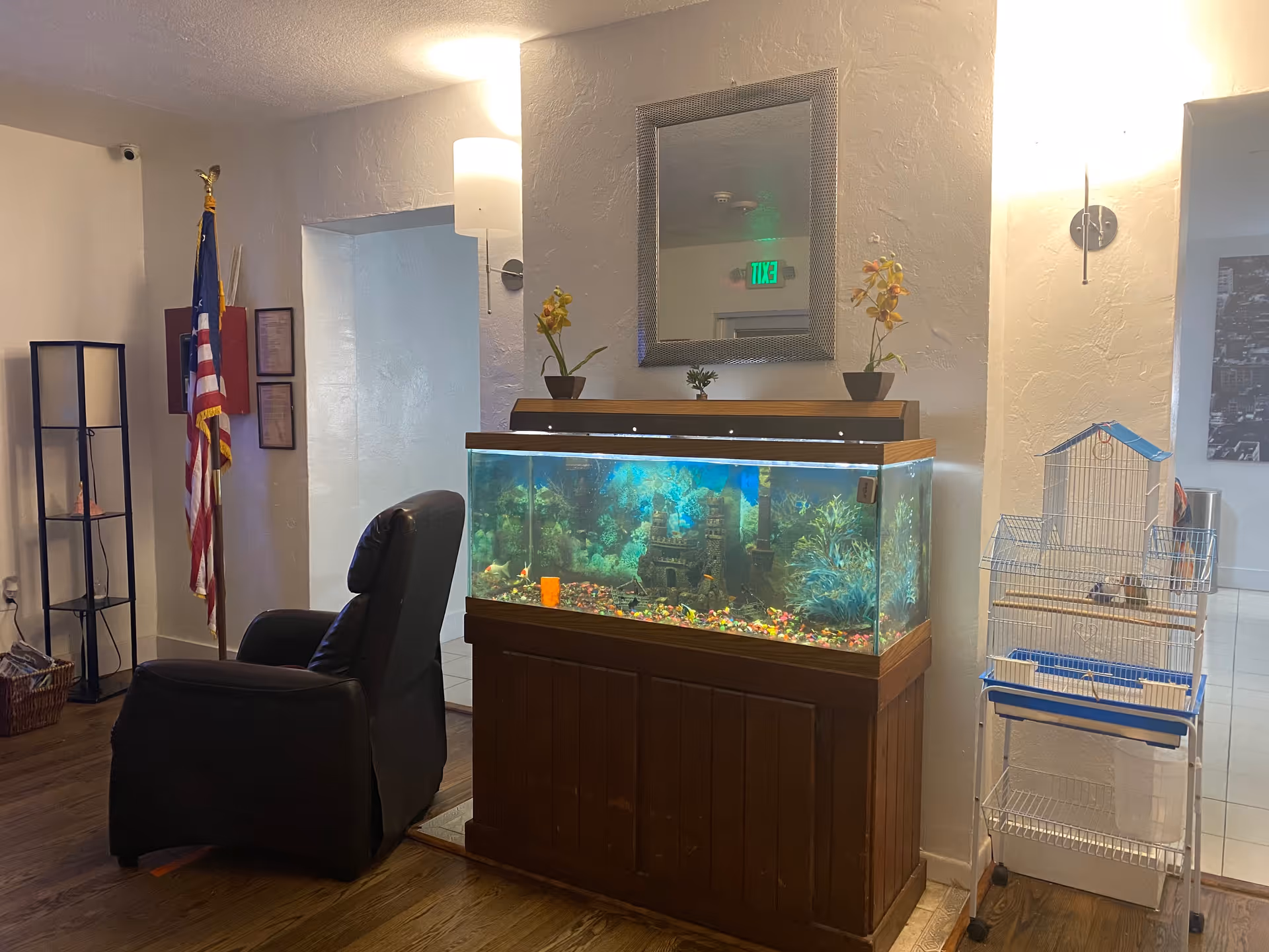 Interior common area showing a large aquarium on a wooden stand, a recliner, American flag, birdcage, and wall mirror.