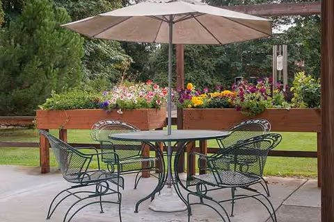 Outdoor patio with round table, chairs, umbrella, and vibrant flower planters.