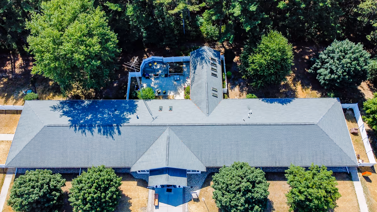 Aerial view of a single-story senior living facility building surrounded by trees and greenery, with a patio area visible at the back of the building.