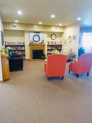 Communal living room with upholstered chairs, bookshelves and a fireplace.