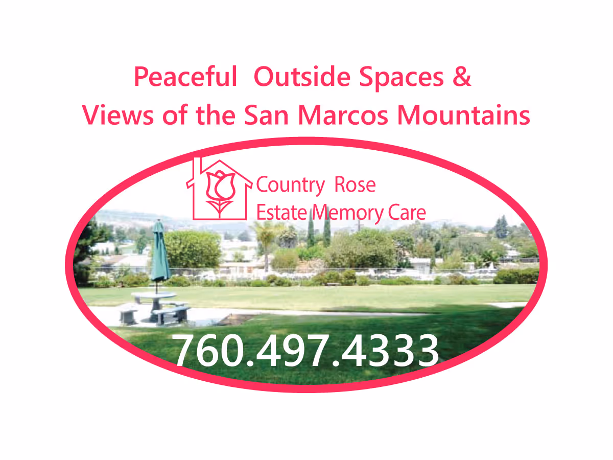 Outdoor area with green grass, a picnic table with an umbrella, and a view of trees and the San Marcos Mountains in the background.