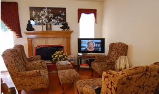 Cozy living room with patterned armchairs arranged around a fireplace and a small TV on a stand.