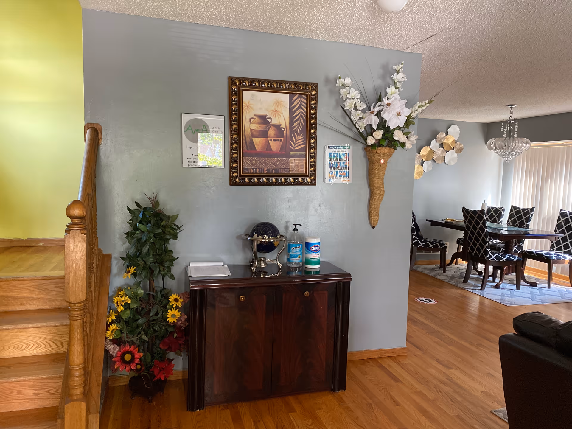 Entry area with a wooden staircase, decorative cabinet and wall art leading into a dining room with a table and chairs.