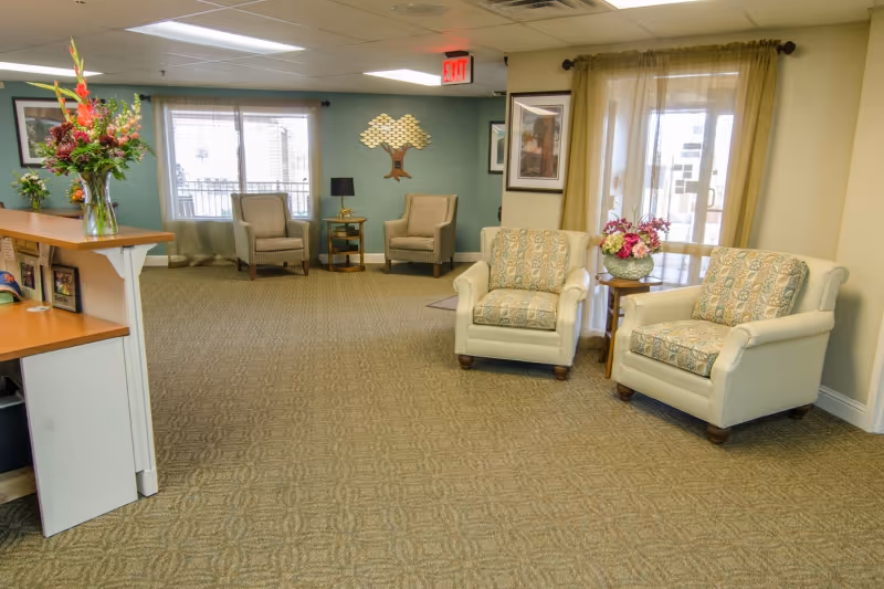 Open reception lounge with upholstered armchairs, side tables, floral arrangements, and a front desk area.