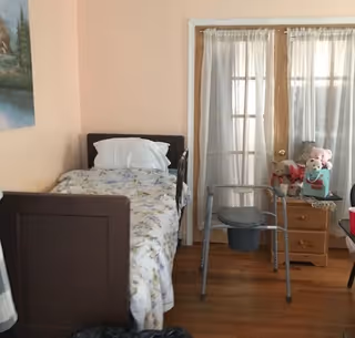 Small bedroom with a single bed, walker, and dresser in a pastel-toned room.