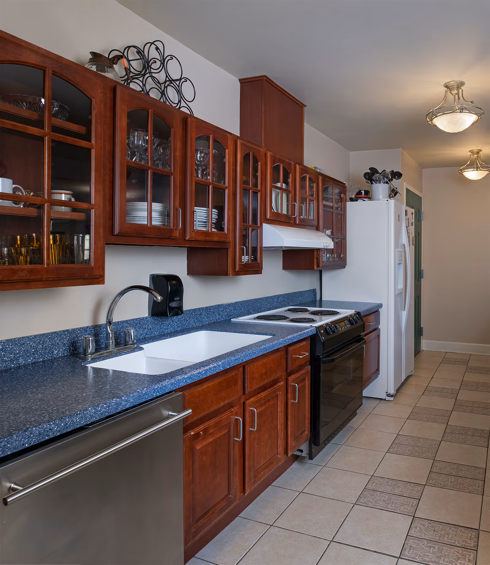 Galley-style kitchen with dark wood cabinets, blue speckled countertops, a sink, stove, and refrigerator.