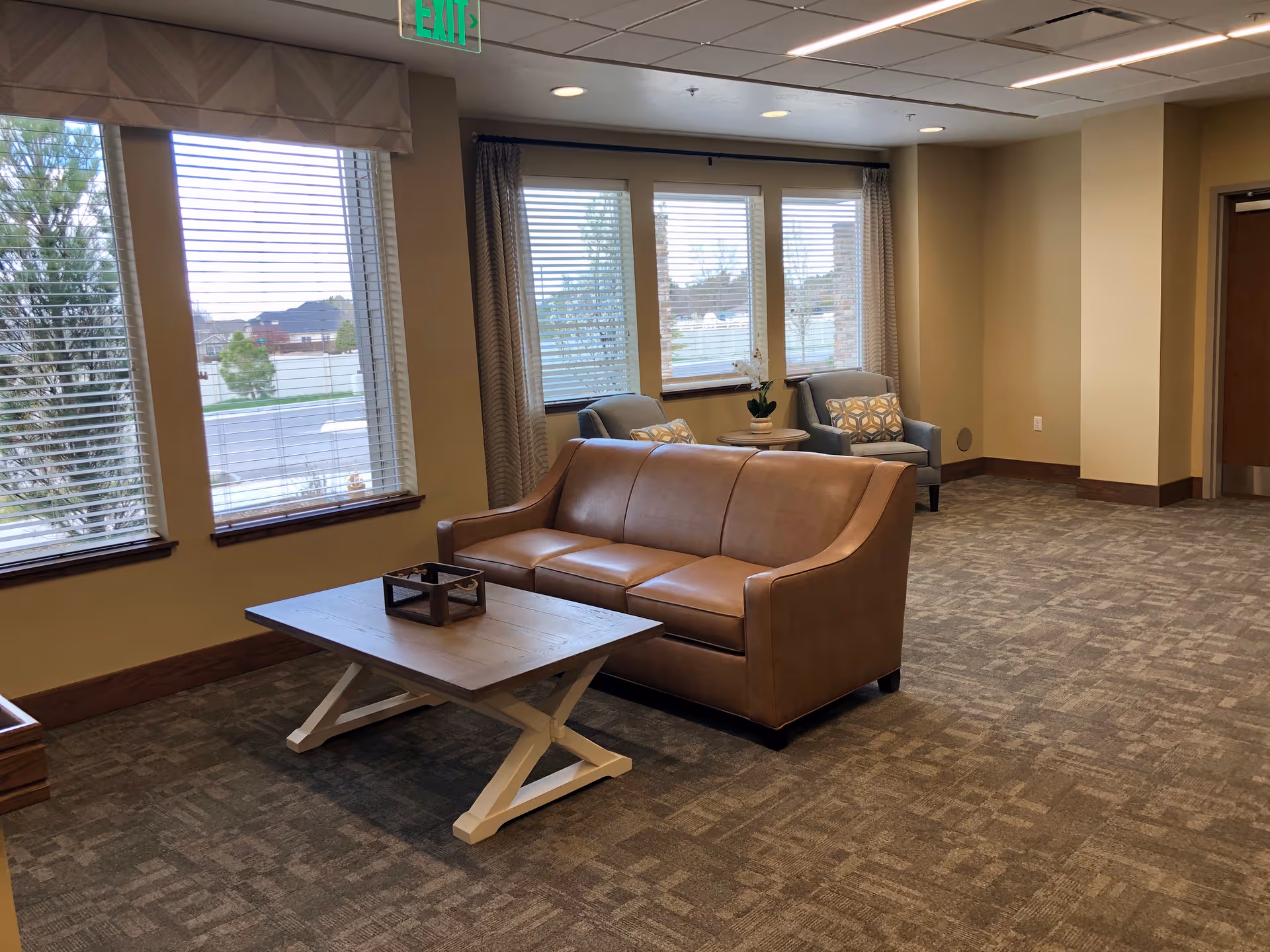 Seating area in an assisted living facility with a leather sofa, coffee table, armchairs and large windows.