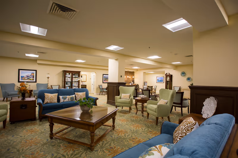 Spacious furnished senior living common lounge with sofas, armchairs, coffee tables, and decorative accents.