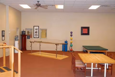 Rehabilitation room with parallel bars, exercise mats, therapy equipment, and a table.