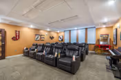 Community media room with two rows of black leather reclining chairs, a popcorn machine, piano, and wall decor.