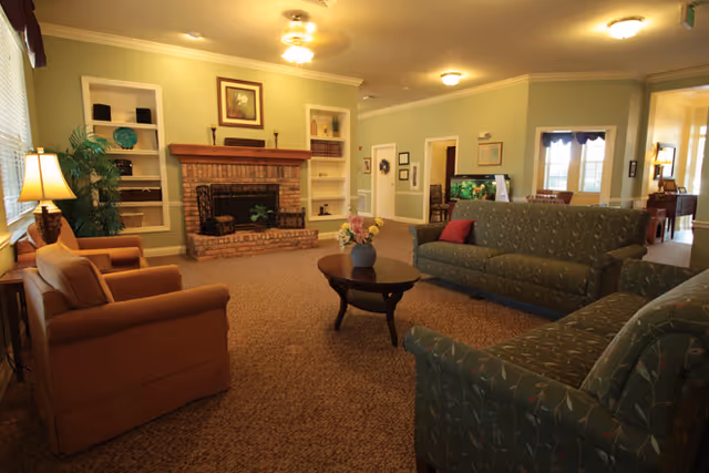 Cozy common living room with sofas and armchairs arranged around a central coffee table facing a brick fireplace and built-in shelving.