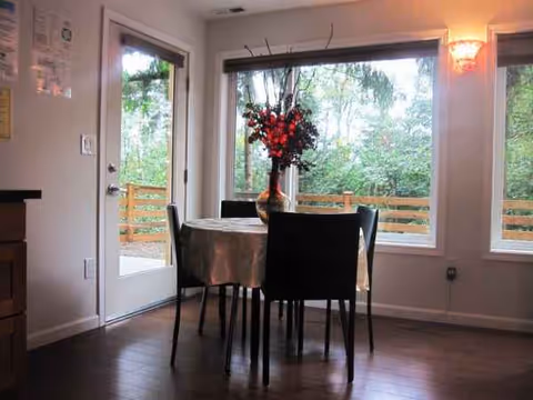 Round table with a flower centerpiece, four chairs, and windows overlooking a deck