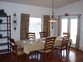 A dining room with a long table, wooden chairs, chandelier, and windows.
