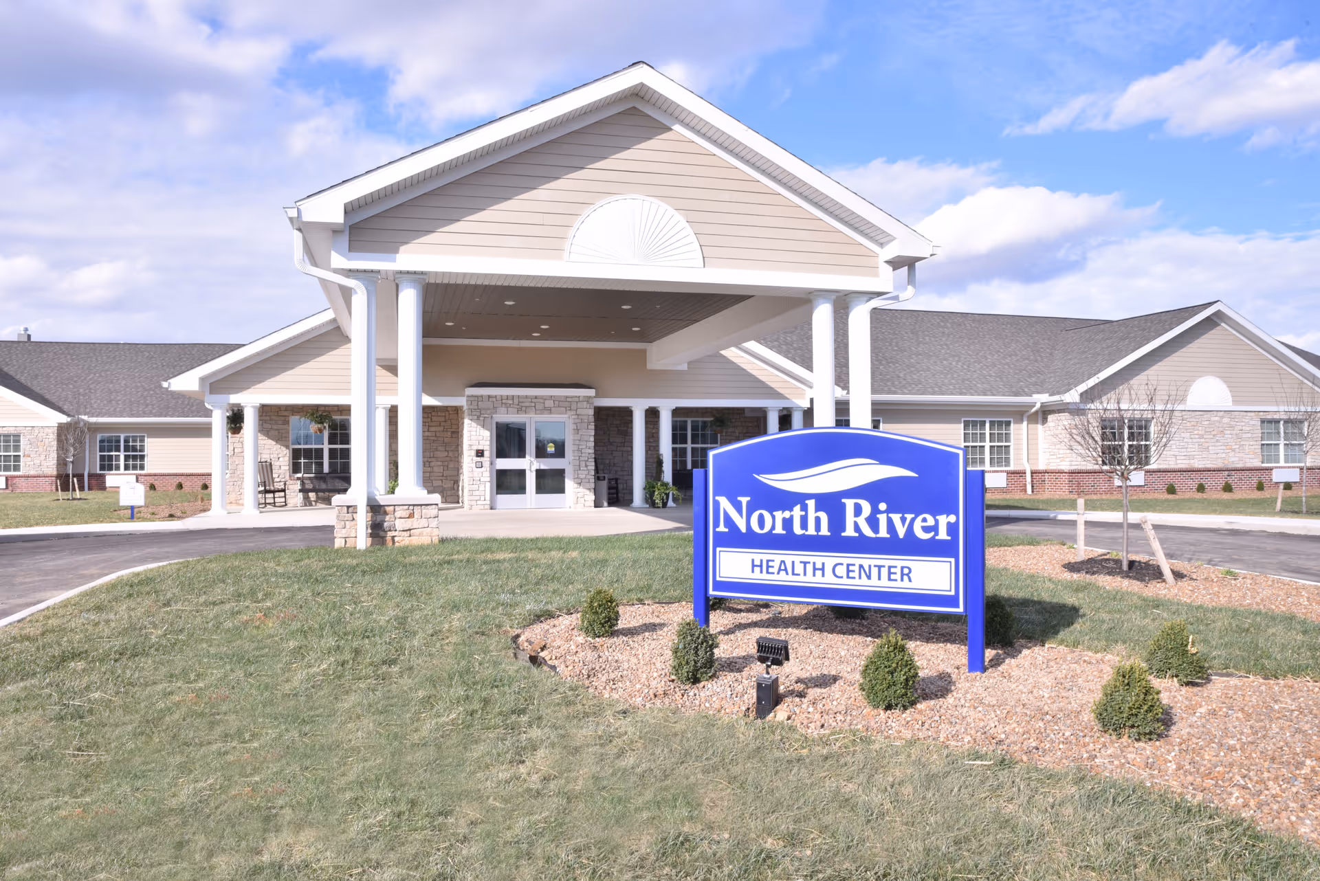 Front entrance of North River Health Center with a blue sign on the lawn.