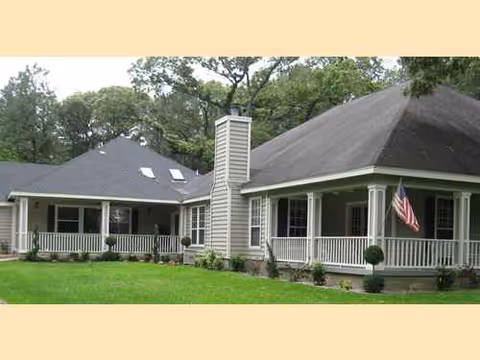 A single-story senior living facility with a wraparound porch and an American flag.