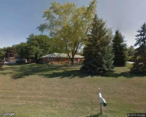 Exterior view of Rainbow Terrace facility with lawn, trees, and a brick building.