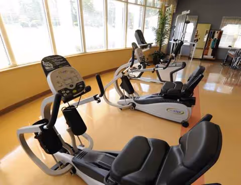 Bright interior fitness center with cardio equipment by large windows.