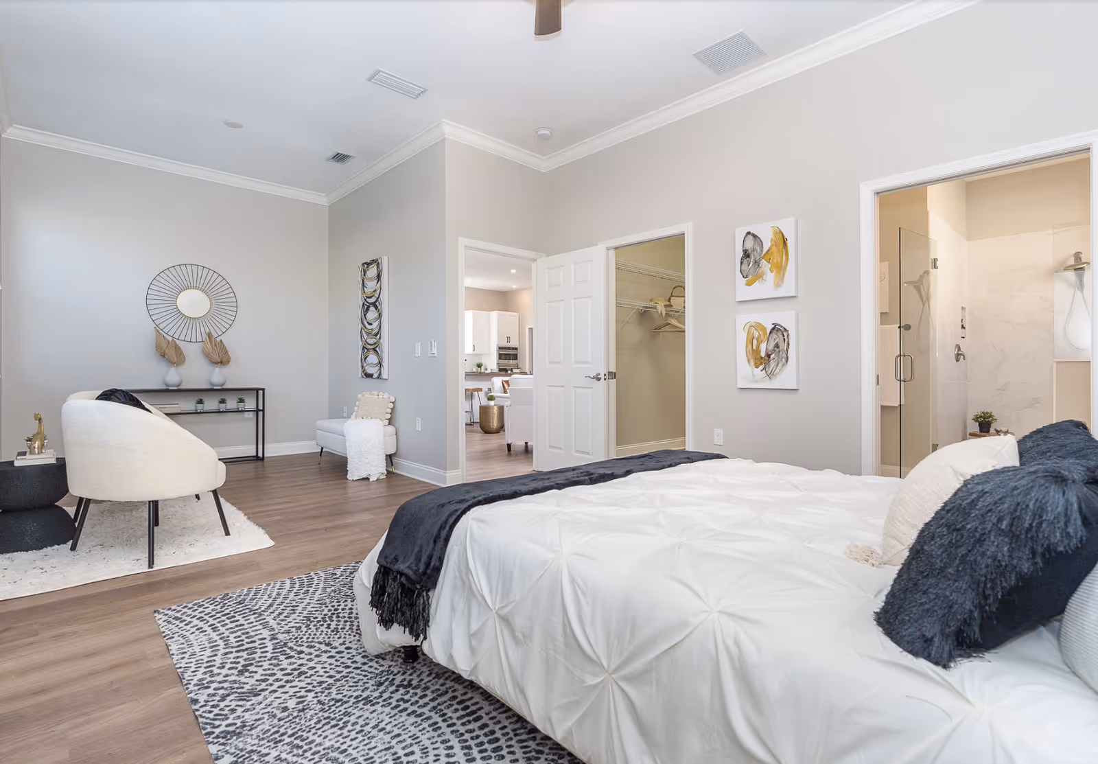 Bright modern bedroom with a bed in the foreground, a seating area, open doors to a walk-in closet and an ensuite bathroom.
