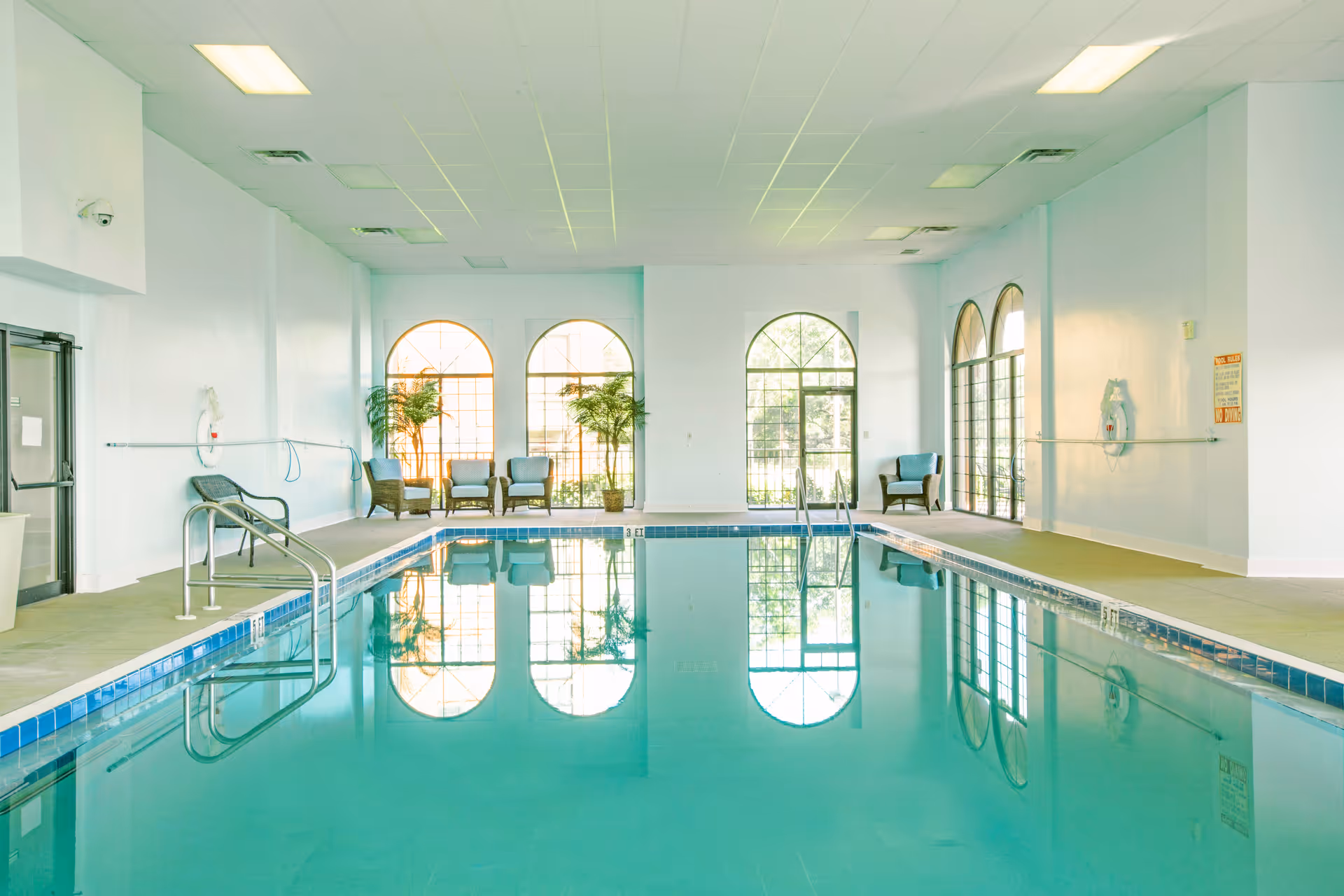 Indoor swimming pool with lounge chairs and arched windows reflected in the water.