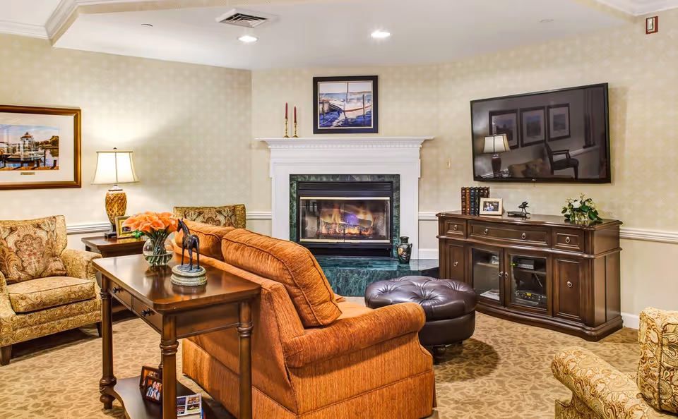 Cozy living room with a sofa and armchairs facing a fireplace and a wall-mounted TV.