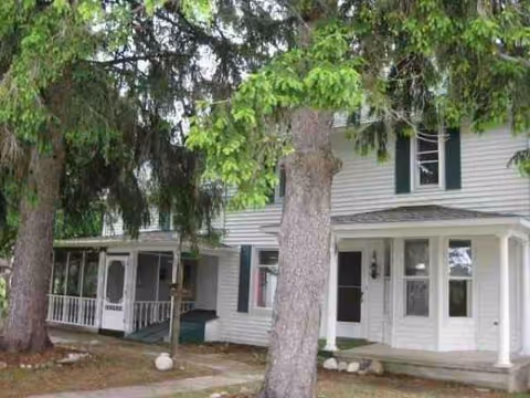 White two-story senior living house with front porch, green shutters, and large trees.