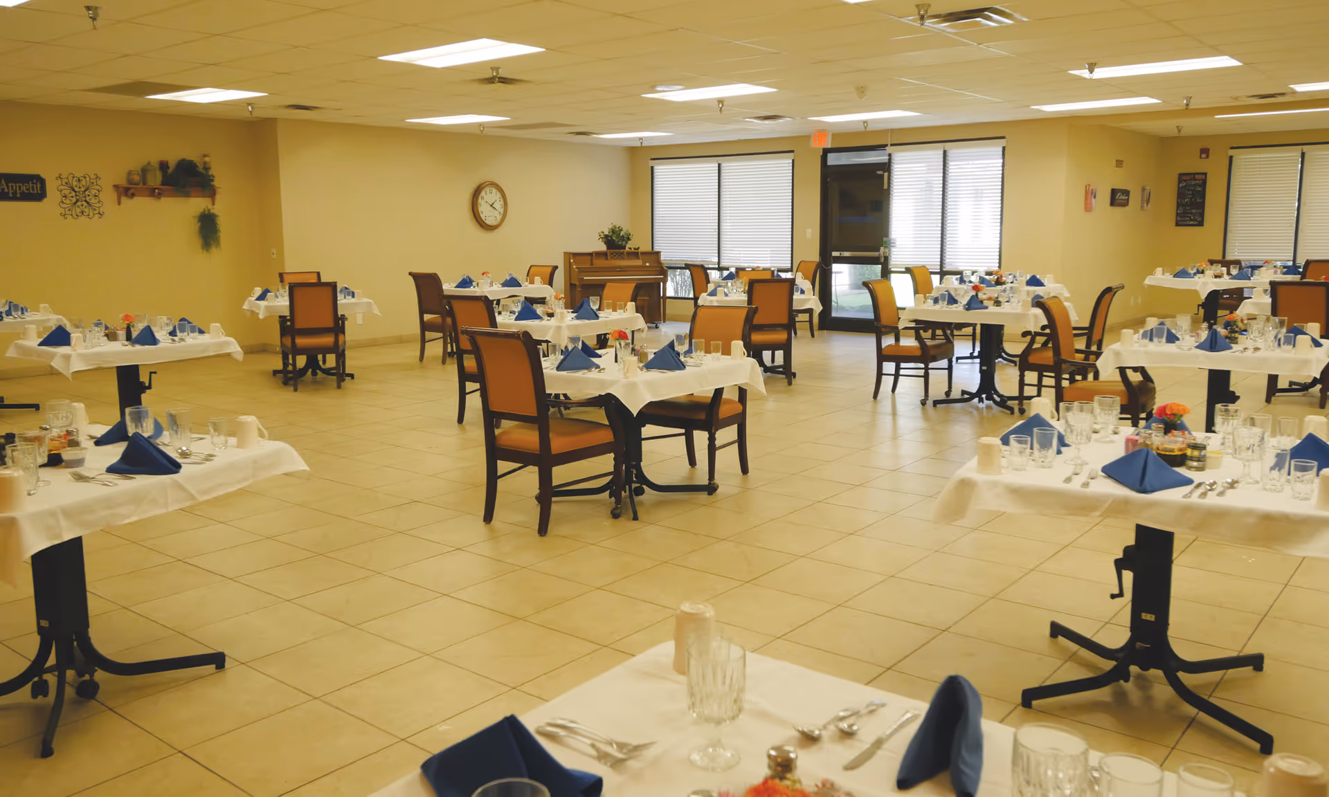 Spacious dining room with multiple tables set with white tablecloths, blue napkins, and chairs.
