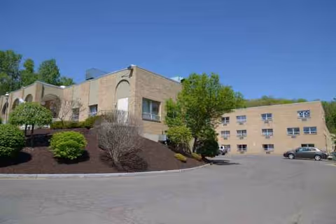 Exterior view of a beige senior living facility with landscaped hill and parking lot.