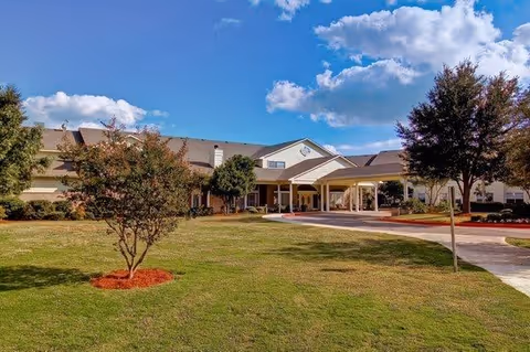Exterior view of The Waterford at Thousand Oaks facility showing a large green lawn with a few trees and a two-story building under a partly cloudy sky.