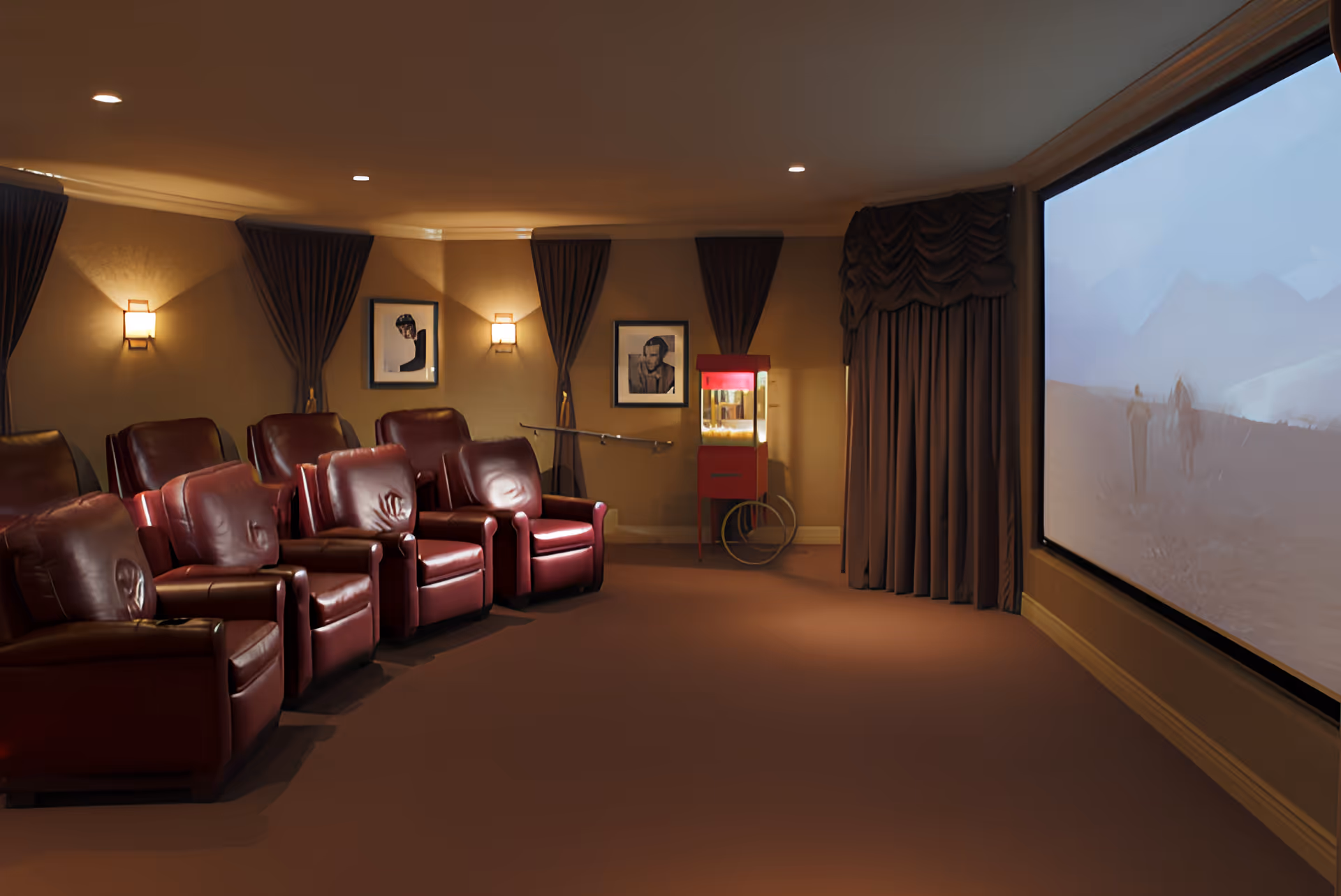 A small theater room with rows of red leather recliners facing a large projection screen and a popcorn machine.