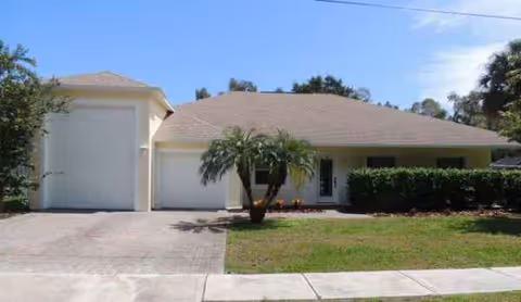 Single-story beige house with two-car garage, palm tree, and manicured lawn.