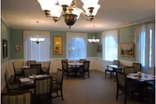 Senior living dining room with striped chairs, tables, lamps, and large windows.