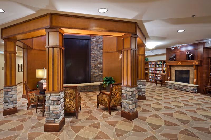 Community lounge with a wood-paneled seating pavilion, patterned carpet, fireplace and bookshelves.