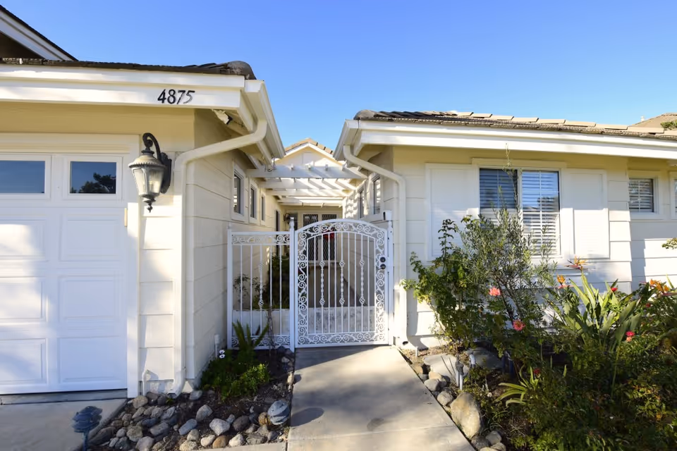 White single-story house front with a decorative white metal gate between the garage and main entrance, house number 4875 visible.