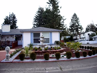 Front exterior of a single-story care home with a circular fountain and landscaped yard.