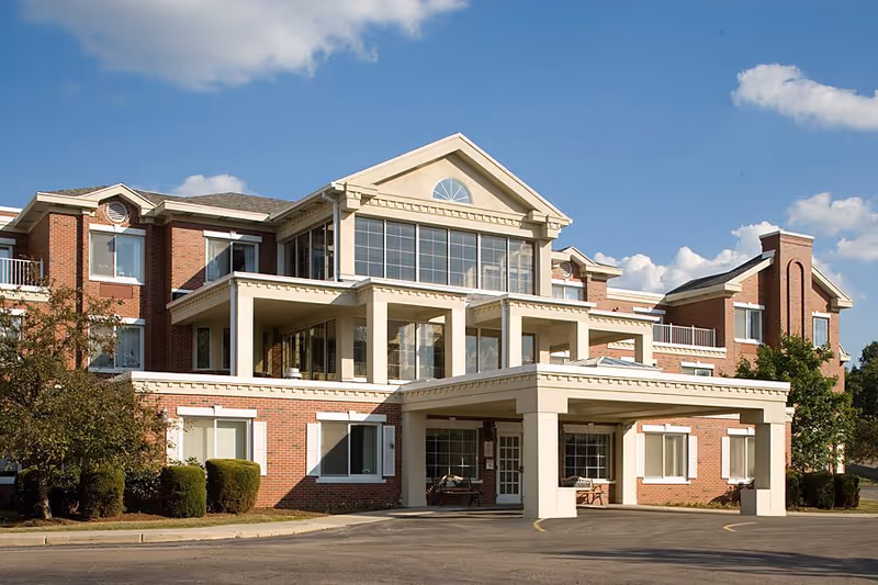 Front exterior of a three-story brick nursing center with a covered entrance and large windows under a blue sky.