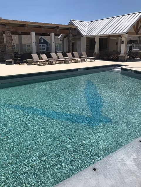 Clear outdoor swimming pool with lounge chairs, pergola and a covered pavilion at a senior living community.