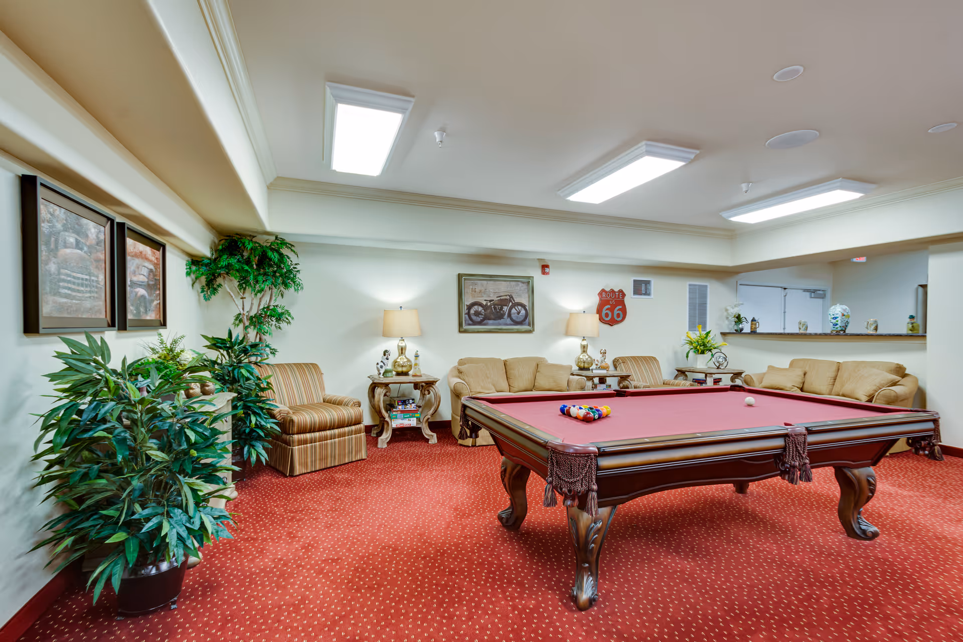 Cozy indoor lounge with a red-felt pool table, sofas and chairs, potted plants, and wall décor.