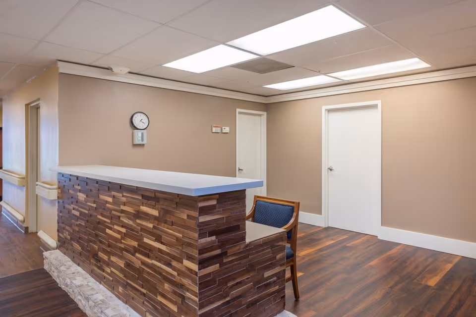 Empty reception area with a wood-paneled counter, a chair, a clock on a beige wall and two white doors.