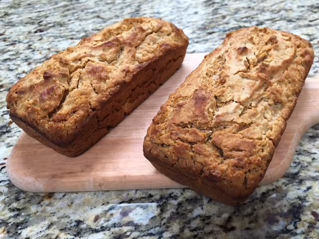 Two freshly baked loaves of bread placed on a wooden cutting board on a granite countertop.