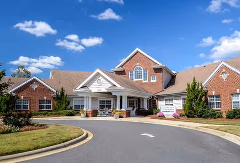 Trinity Village senior living facility entrance with brick exterior, curved driveway, and landscaped grounds.