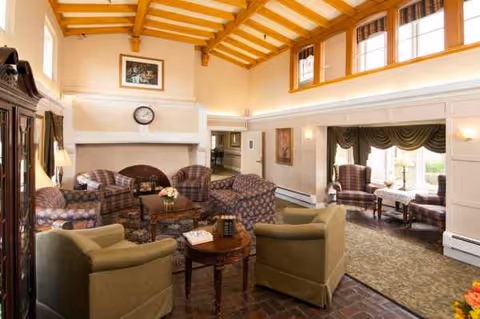 Spacious senior living lounge with wooden-beamed ceiling, sofas, chairs, and a fireplace.