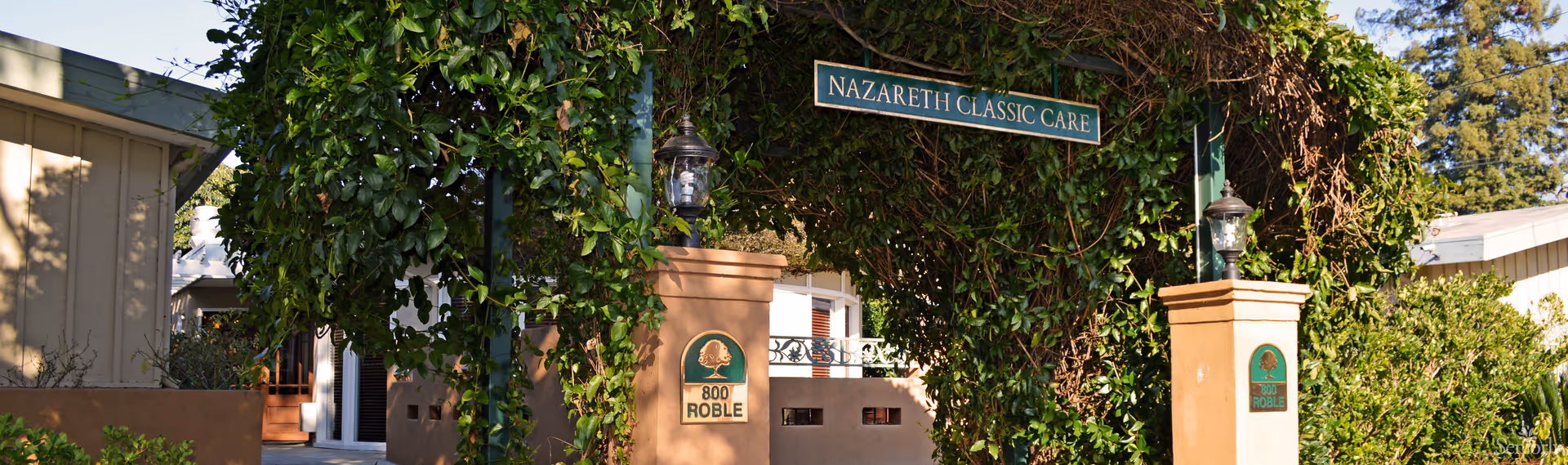 Ivy-covered arched entrance to Nazareth Classic Care with pillars marked '800 Roble' and lanterns.