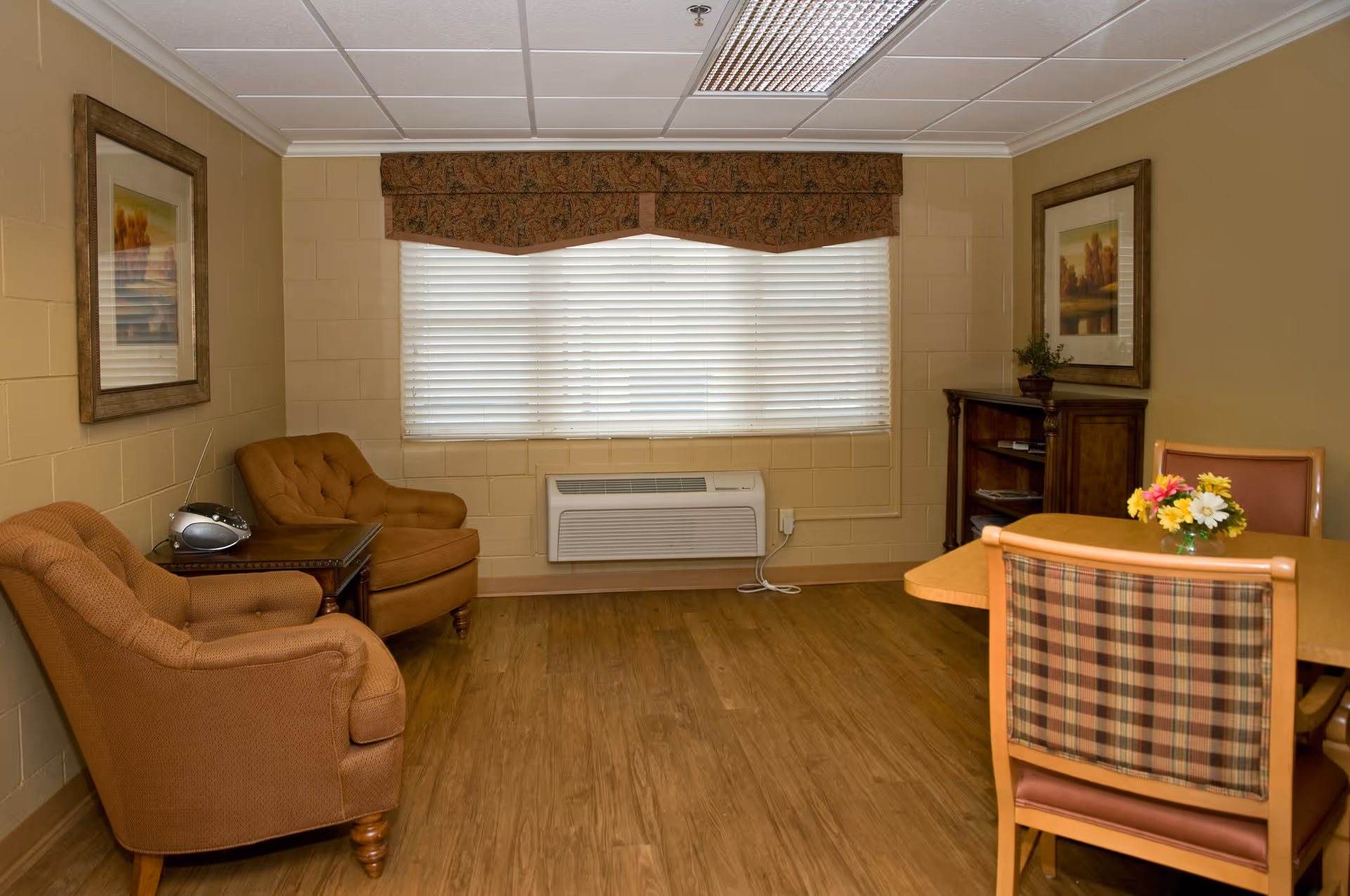 A cozy interior seating area with two armchairs, a table, and window blinds.