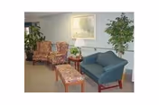 Small sitting area with upholstered chairs, a loveseat, side table with a lamp, and potted plants.
