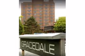 Gracedale Nursing Home sign in foreground with a tall brick building behind and trees.