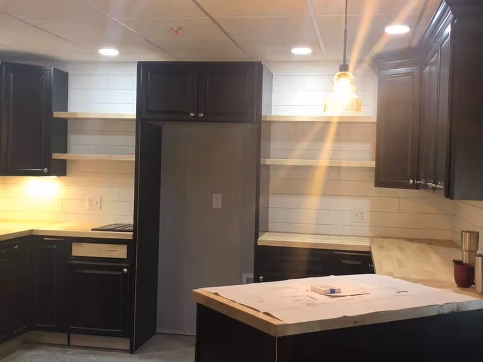 Kitchen with dark cabinets, light wood countertops and open shelving, a central island with papers, and a hanging pendant light.