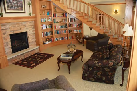 Cozy living room with a fireplace, built-in bookshelves under a wooden staircase, and sofas around a coffee table.