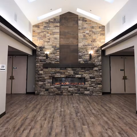 Lobby interior featuring a tall stone fireplace wall with an electric firebox, skylights, and wood-look flooring.