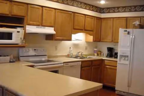 Kitchen in a senior living facility with wooden cabinets, a white refrigerator, stove, and island counter.